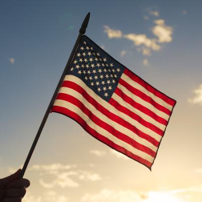 American flag against blue sky with sun and some clouds